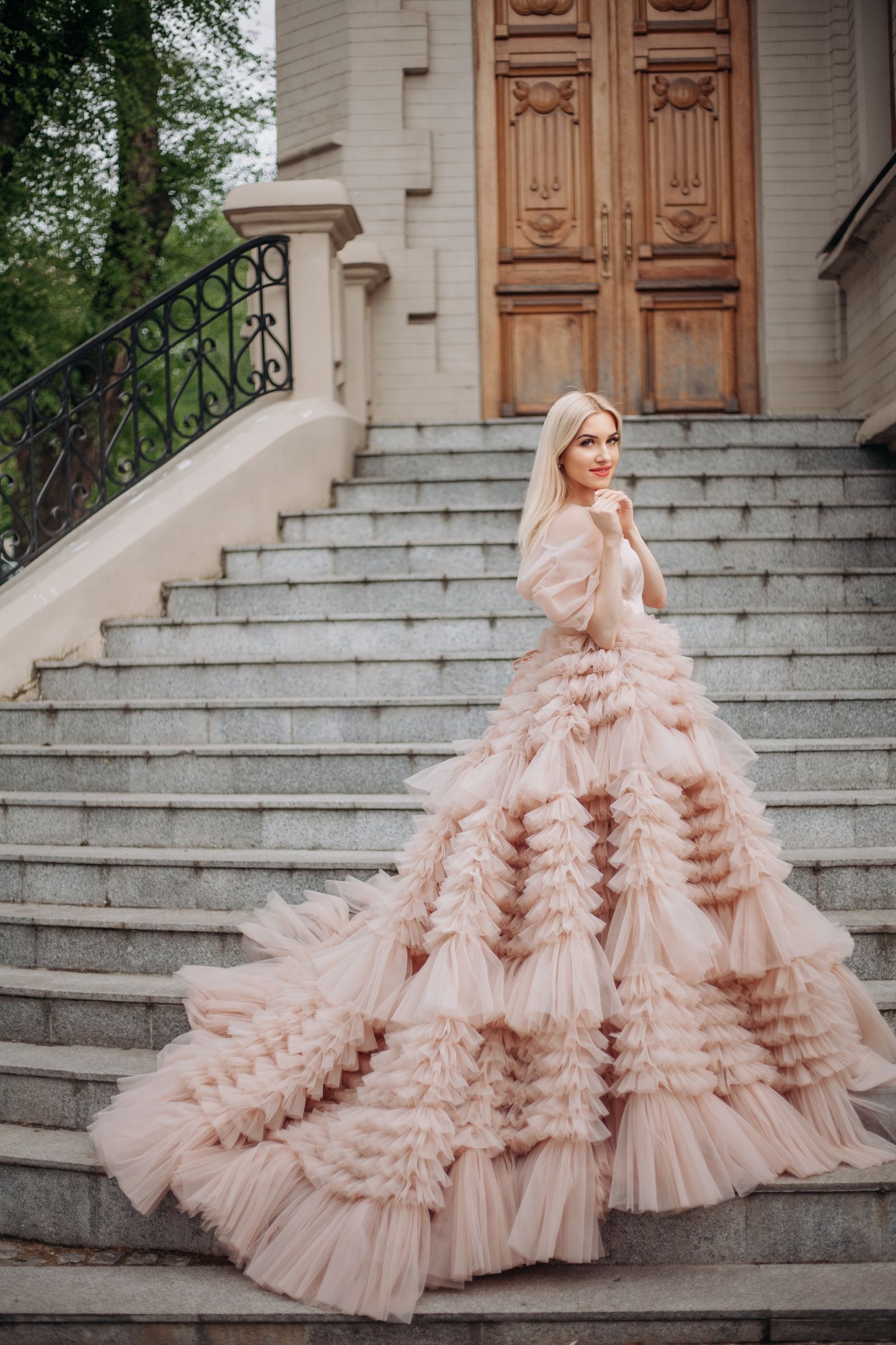 A blush tulle ball gown with a ruffled train on a grand staircase